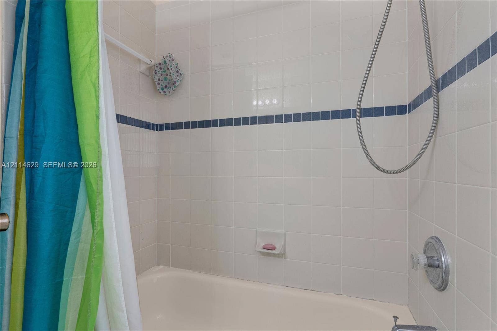 Bathtub enclosure featuring white square wall tile, blue accent tile trim, integrated soap dish, and a handheld shower fixture