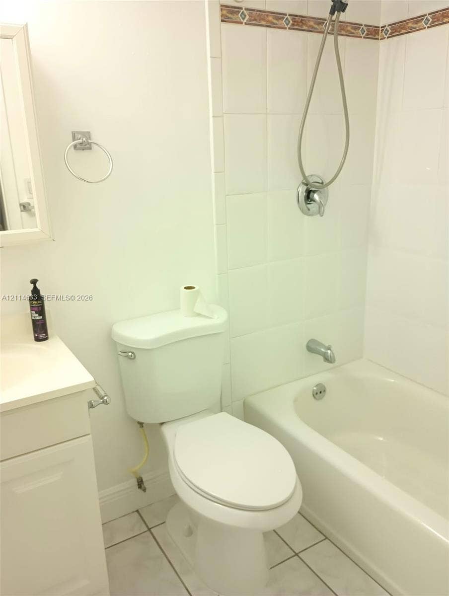 Bathroom featuring a vanity with an integrated basin, white tile surround, tub-shower combination, and tiled flooring