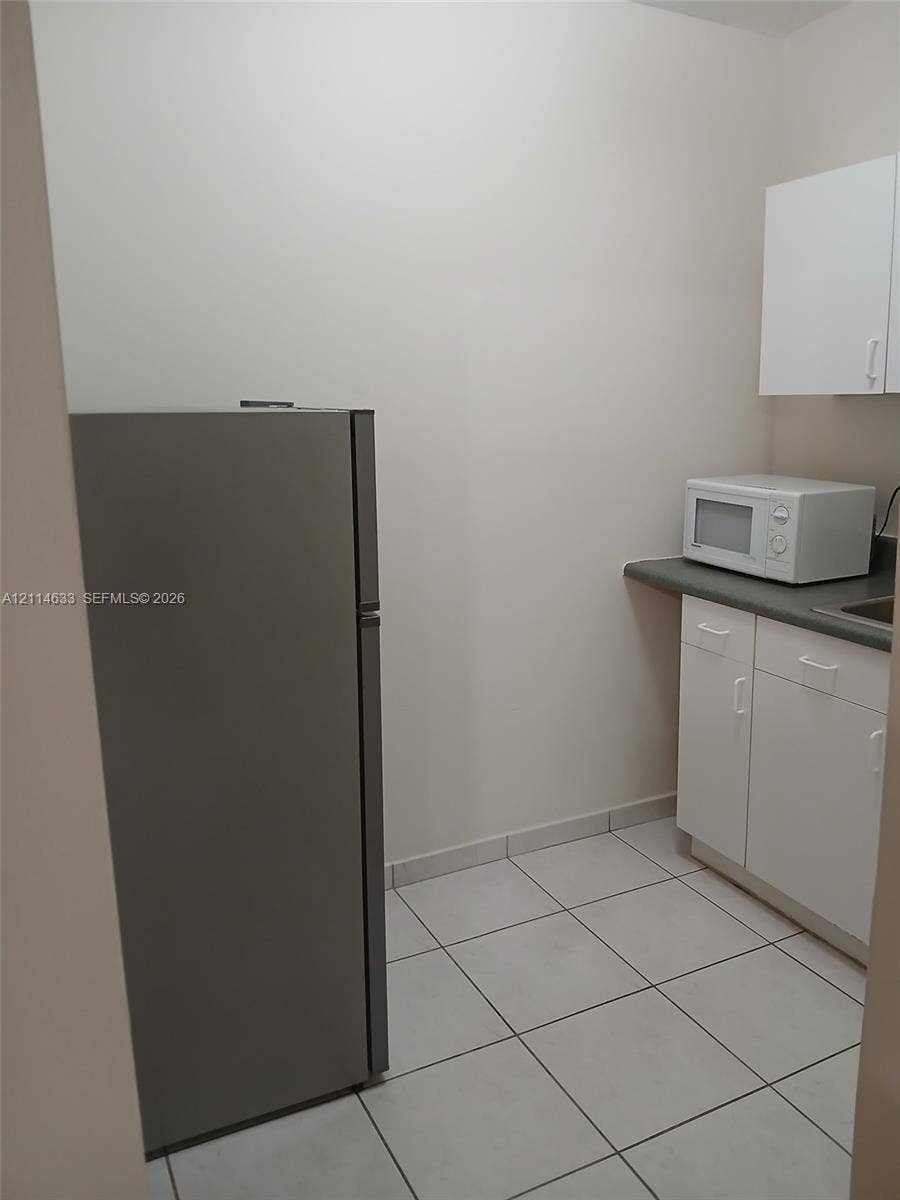 Stainless steel refrigerator, white cabinetry, solid-surface countertops, and tiled flooring