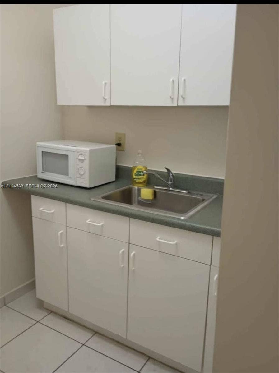 Kitchenette featuring white cabinetry, neutral-toned solid surface countertop, stainless steel sink, and chrome finish faucet