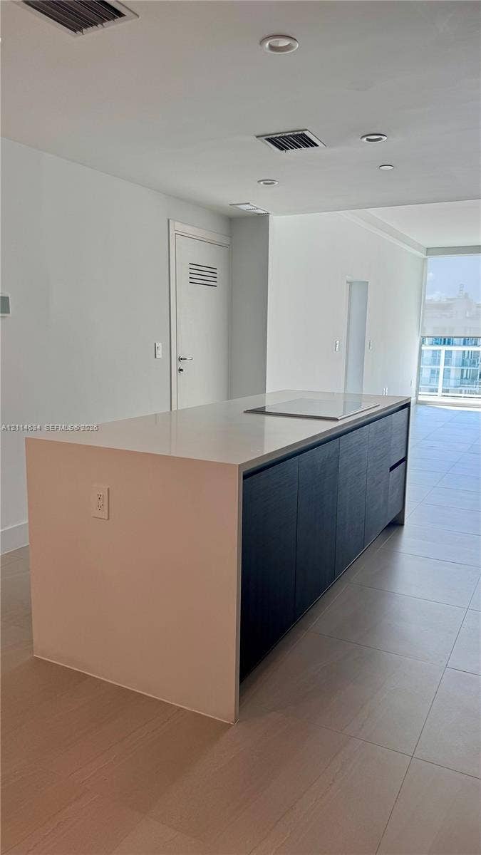 1150 102nd Street, #704, Bay Harbor Islands, Bay Harbor Islands, FL 33154 Kitchen island featuring a solid-surface countertop with an integrated cooktop and dark-finish cabinetry