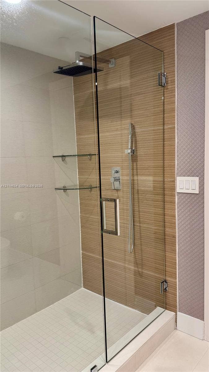 1150 102nd Street, #704, Bay Harbor Islands, Bay Harbor Islands, FL 33154 Walk-in shower featuring a glass enclosure, rainfall showerhead, handheld sprayer, horizontal-set tile wall accents, and built-in glass shelving