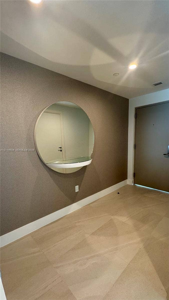1150 102nd Street, #704, Bay Harbor Islands, Bay Harbor Islands, FL 33154 Large-format tile flooring, textured accent wall, and circular wall-mounted mirror with an integrated glass shelf