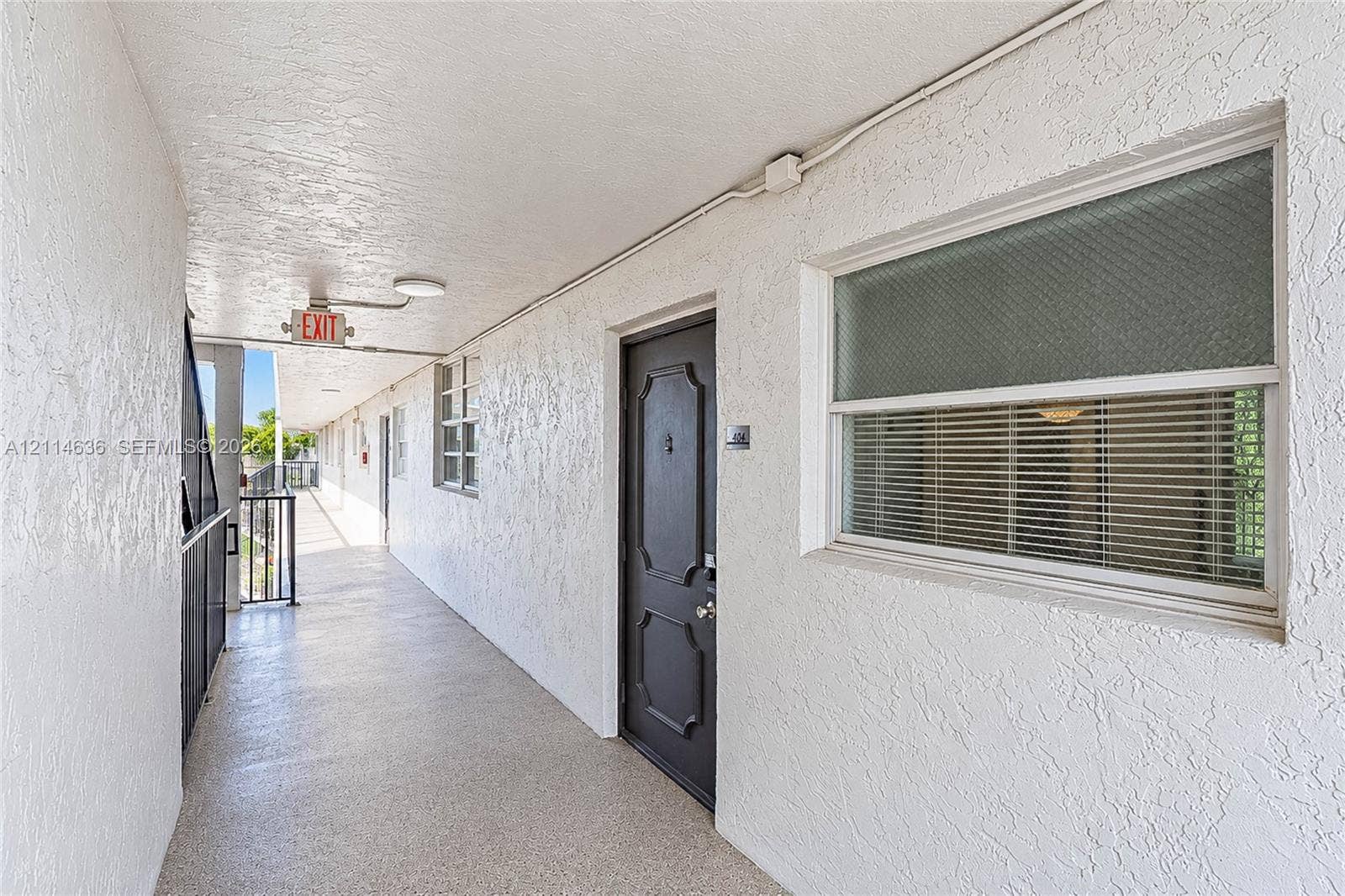 14155 SW 87th Street, #404-E, Miami, Miami, FL 33183 Exterior corridor featuring textured stucco walls, a paneled entry door, window with integrated blinds, and metal railing