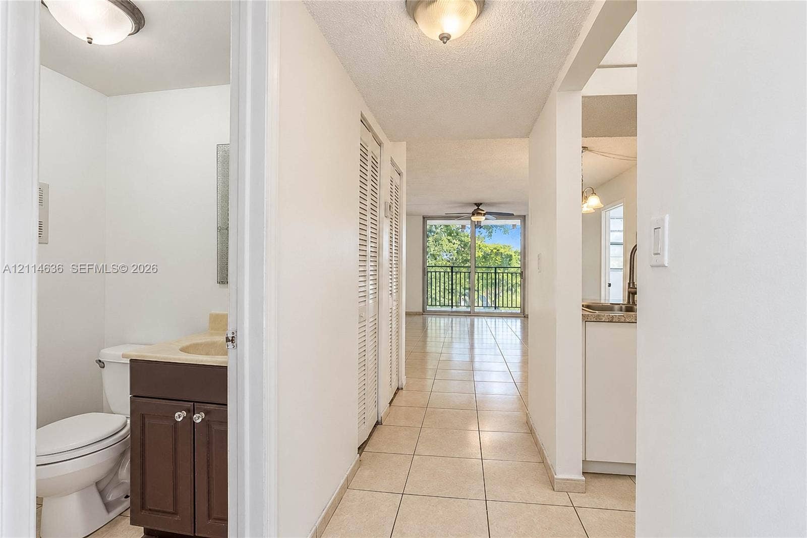 14155 SW 87th Street, #404-E, Miami, Miami, FL 33183 Hallway featuring neutral tile flooring, louvered-door closets, a recessed bathroom with a dark wood-finish vanity, and a glass-paneled door opening to a balcony