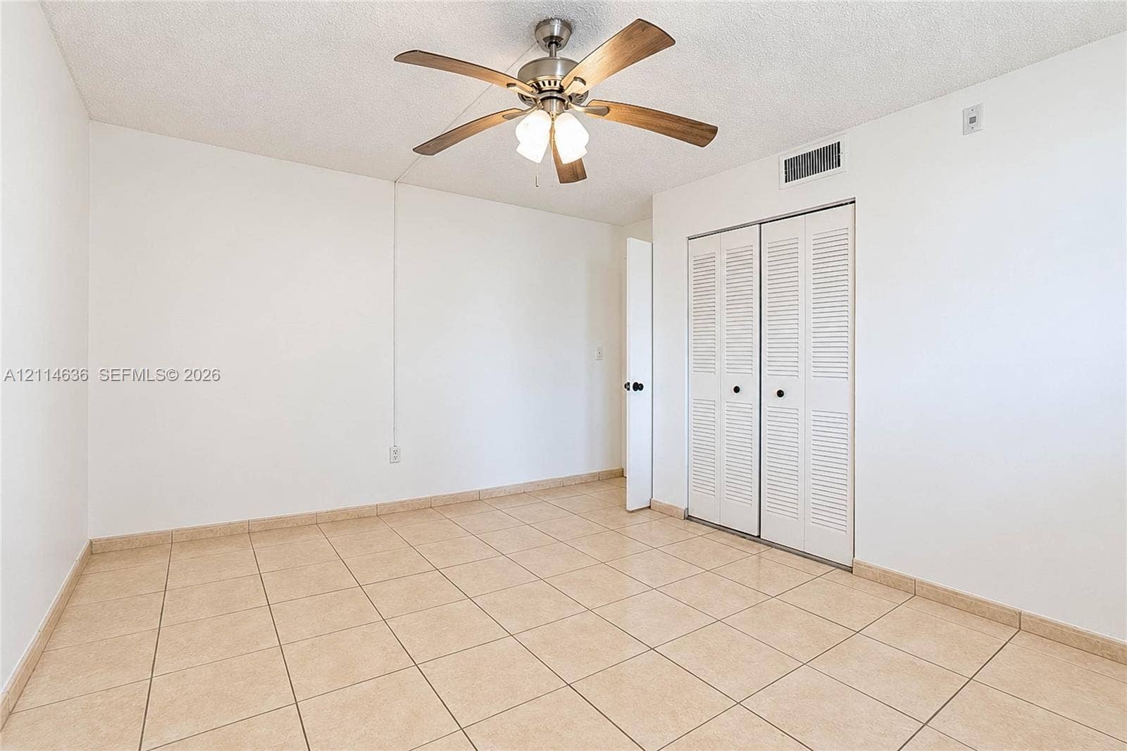 14155 SW 87th Street, #404-E, Miami, Miami, FL 33183 Room featuring neutral ceramic tile flooring, a brushed nickel ceiling fan with integrated lighting, and a closet with white louvered bi-fold doors