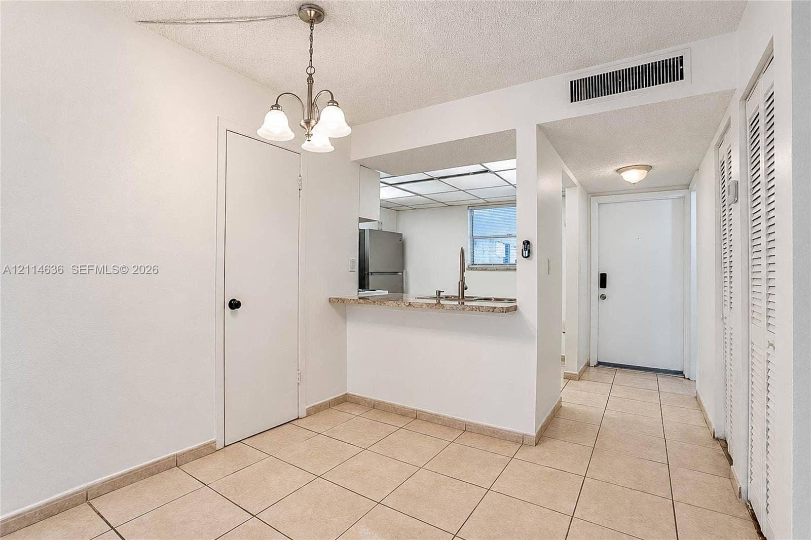 14155 SW 87th Street, #404-E, Miami, Miami, FL 33183 Ceramic tile flooring, three-light chandelier, stone-surface breakfast bar, stainless steel refrigerator, and louvered bi-fold closet doors