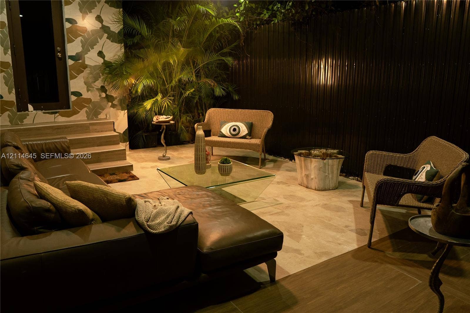 Outdoor patio featuring stone tile flooring, a multi-tiered concrete staircase, patterned exterior wall accent, and metal privacy fencing