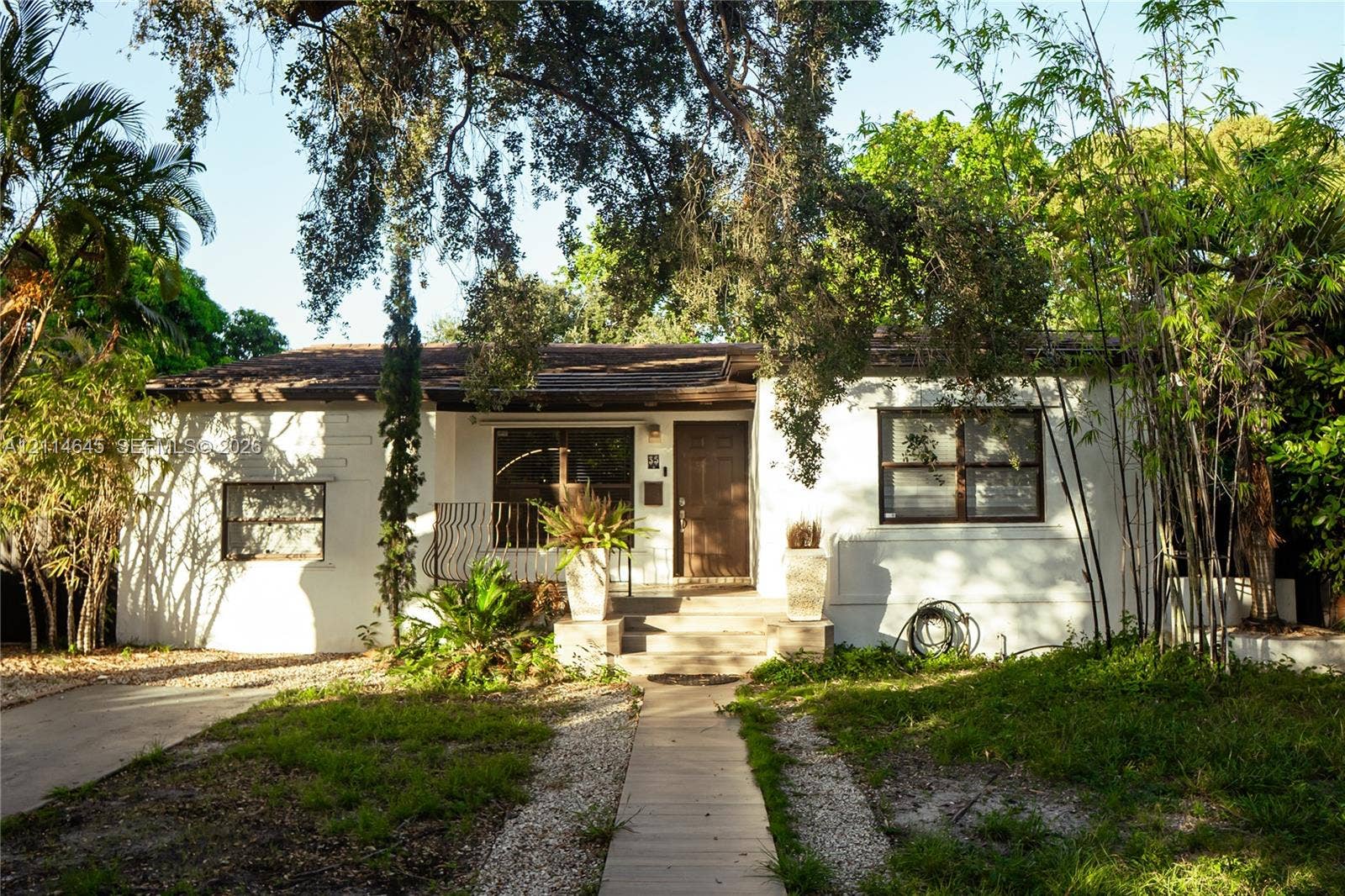 Single-story residence featuring a white stucco exterior, low-pitched roof, concrete front walkway, and mature landscaping