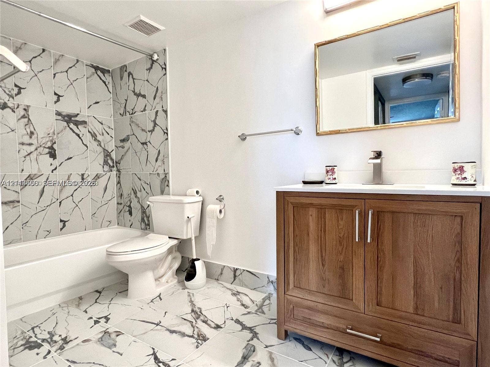 1450 SE 3rd Avenue, #411, Dania, Dania Beach, FL 33004 Bathroom featuring large-format stone-patterned tile flooring, a wood-finish vanity with a white countertop, wall-mounted mirror, and a tub-shower surround accented with coordinating stone-patterned wall tile