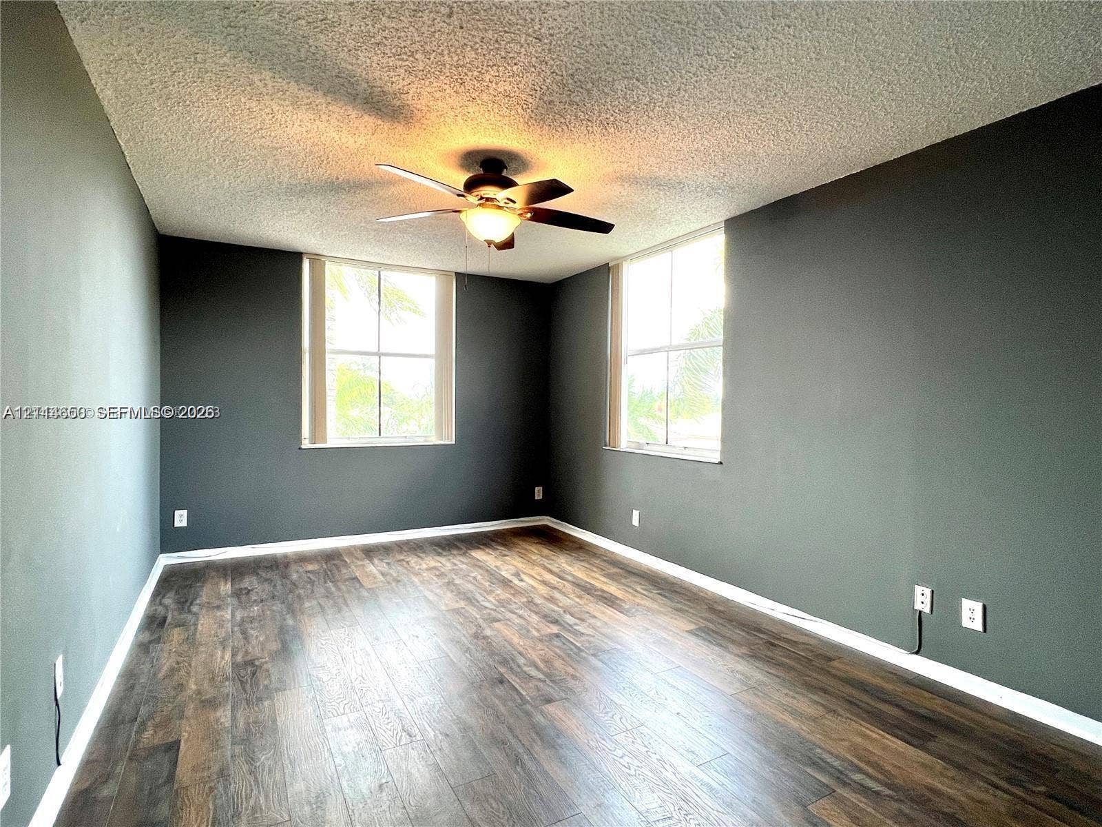 1450 SE 3rd Avenue, #411, Dania, Dania Beach, FL 33004 Room featuring dark-toned walls, wood-finish flooring, two large windows, and a central ceiling fan with integrated lighting