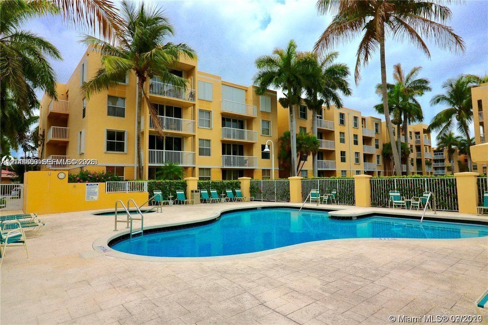 1450 SE 3rd Avenue, #411, Dania, Dania Beach, FL 33004 Swimming pool with integrated spa and stone-paved deck, surrounded by mature palm trees and multi-story residential buildings featuring private balconies