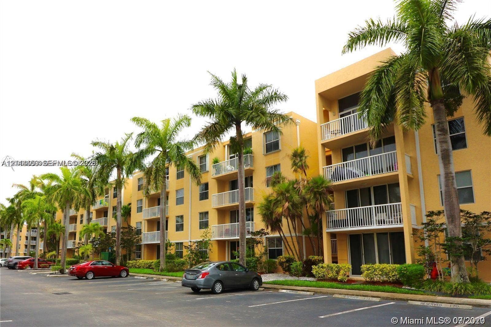 1450 SE 3rd Avenue, #411, Dania, Dania Beach, FL 33004 Multi-story residential building exterior featuring stucco facade, private balconies with white railings, and mature palm tree landscaping