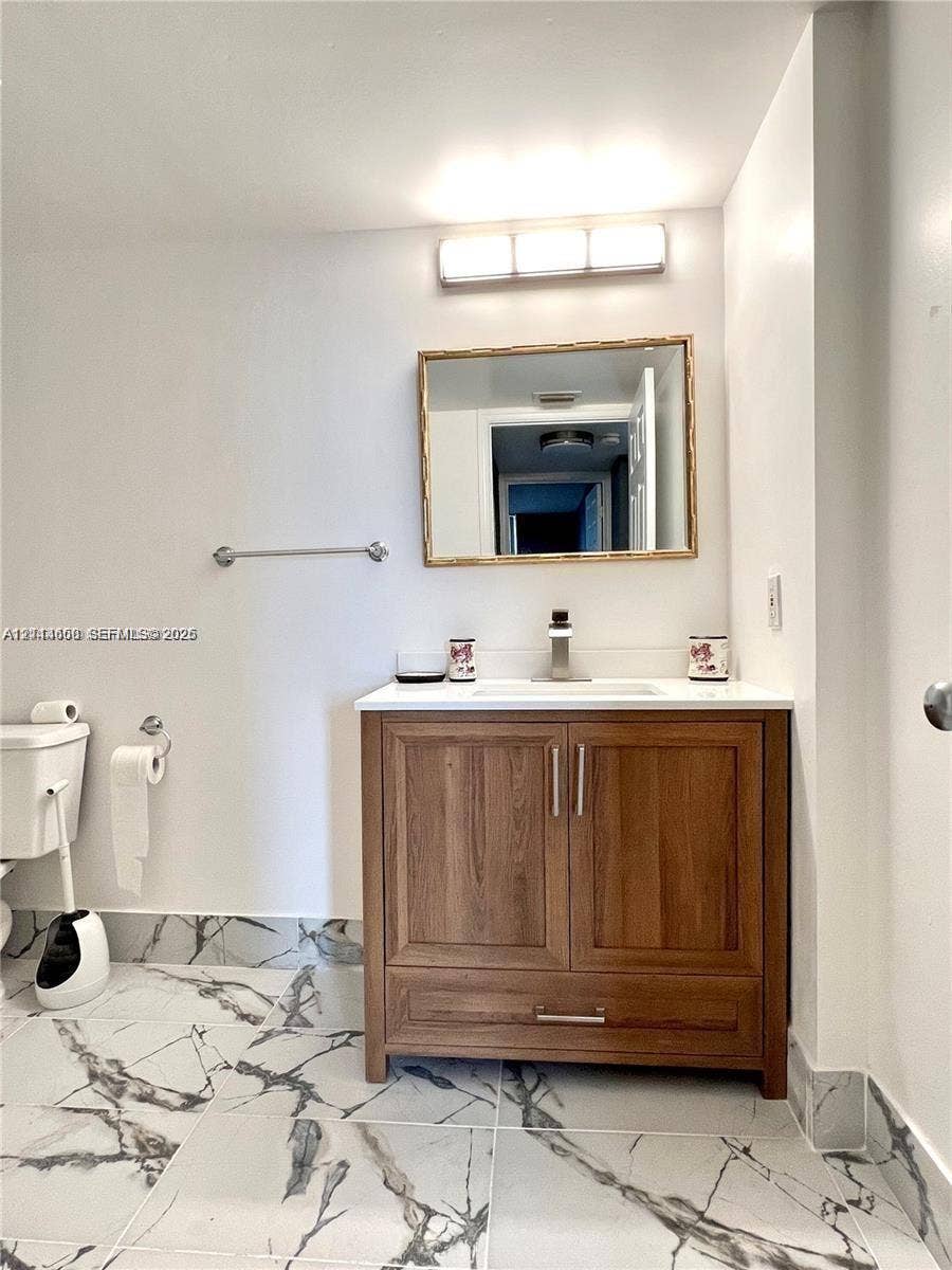 1450 SE 3rd Avenue, #411, Dania, Dania Beach, FL 33004 Wood-finish vanity with a rectangular sink, stone-surface countertop, modern wall-mounted mirror, and large-format veined tile flooring