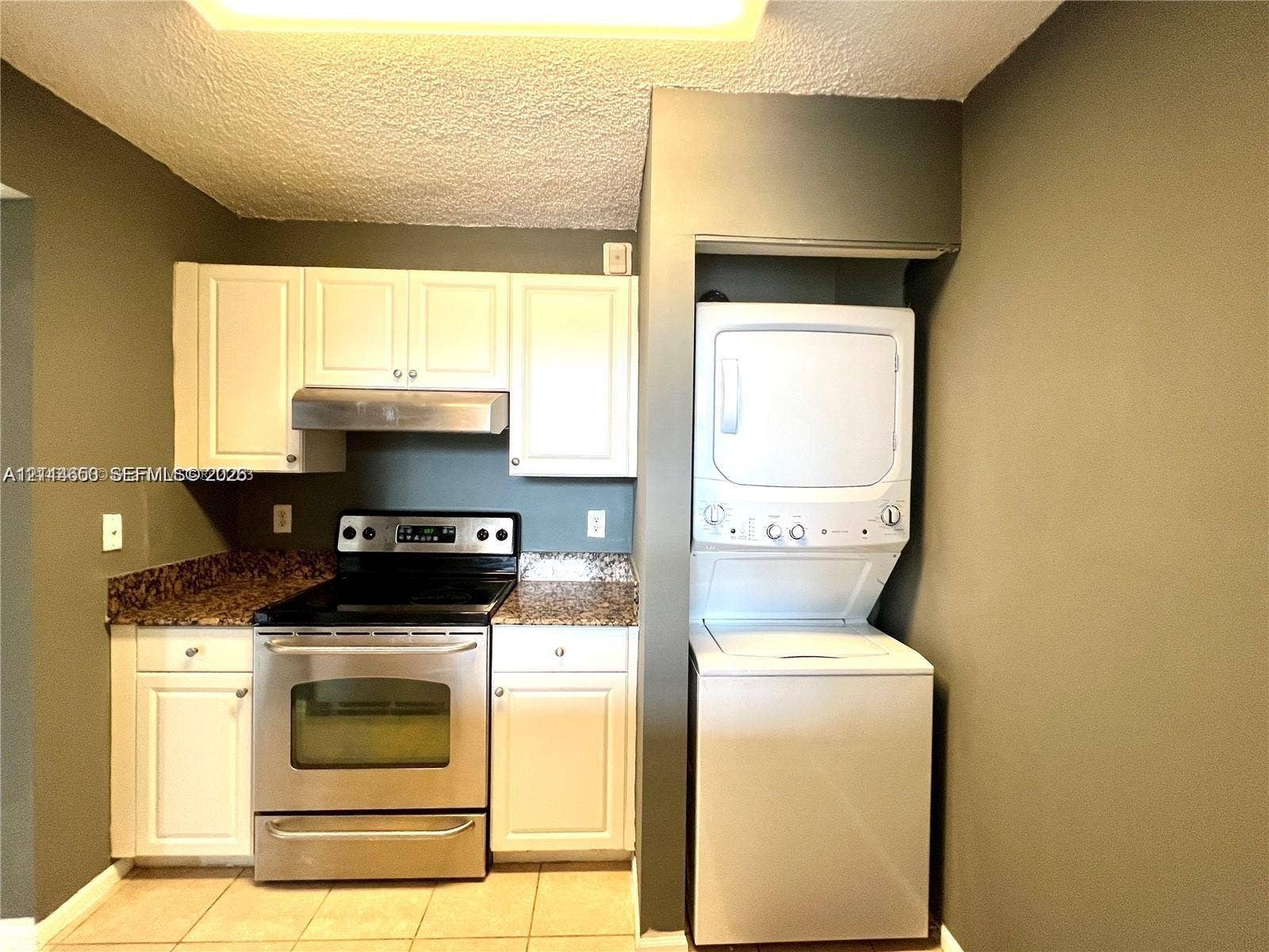 1450 SE 3rd Avenue, #411, Dania, Dania Beach, FL 33004 Kitchen featuring white cabinetry, stone-finish countertops, stainless steel range with integrated hood, and a stacked washer and dryer unit