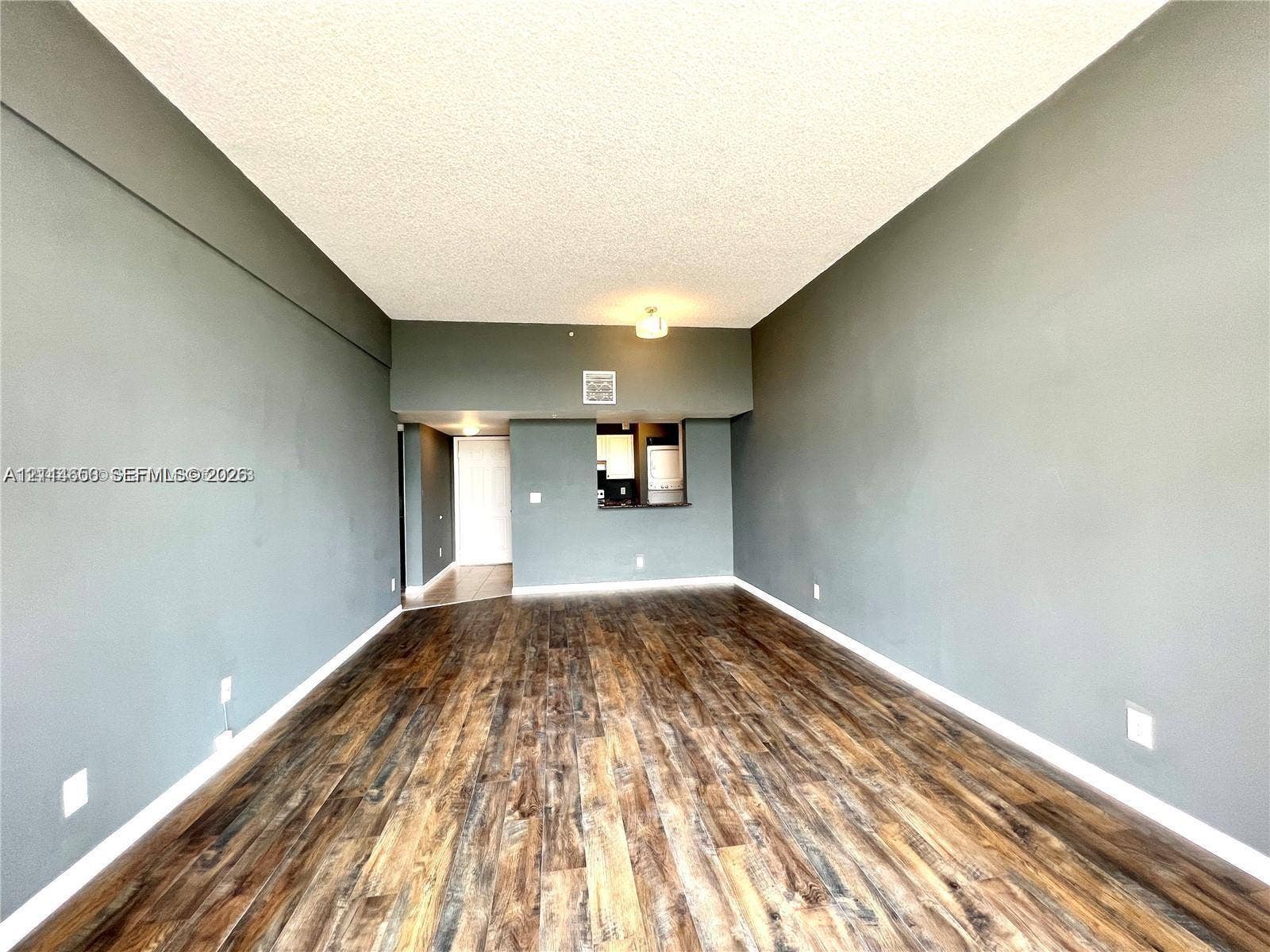 1450 SE 3rd Avenue, #411, Dania, Dania Beach, FL 33004 Open interior space featuring wood-finish flooring, neutral wall tones, and a pass-through opening to the kitchen area