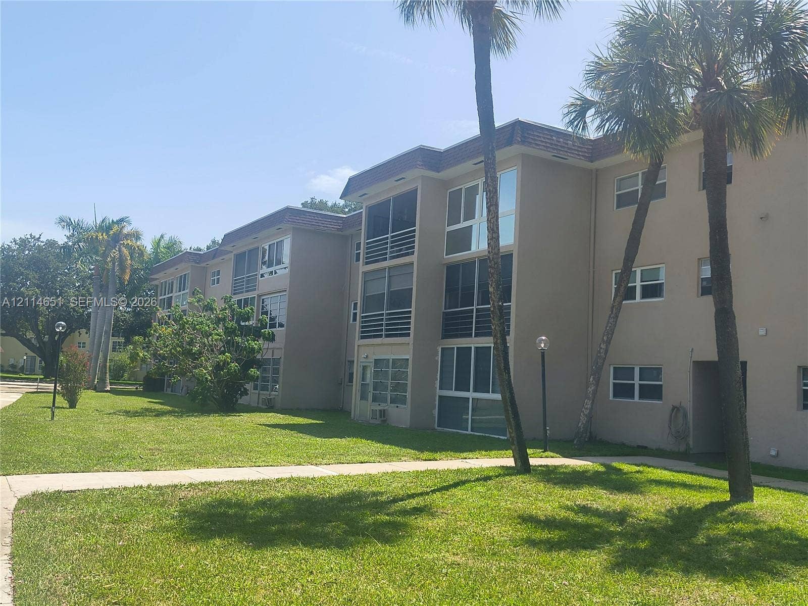 Multi-story stucco exterior featuring screened balconies and mature palm trees