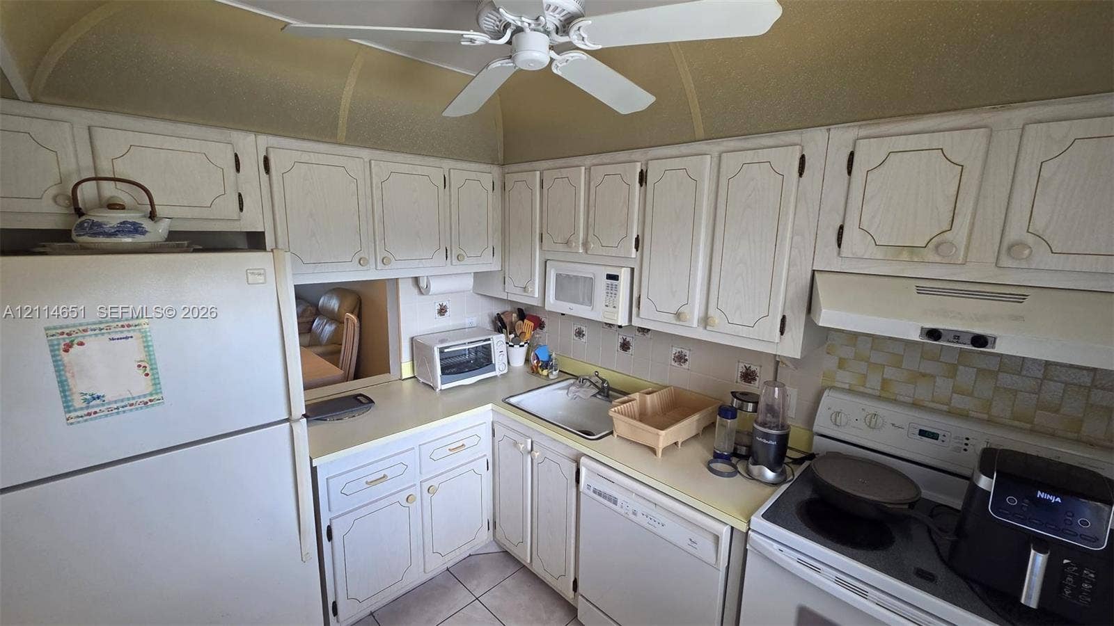 Kitchen featuring white raised-panel cabinetry, light-toned countertops, tile backsplash, built-in microwave, and ceiling fan