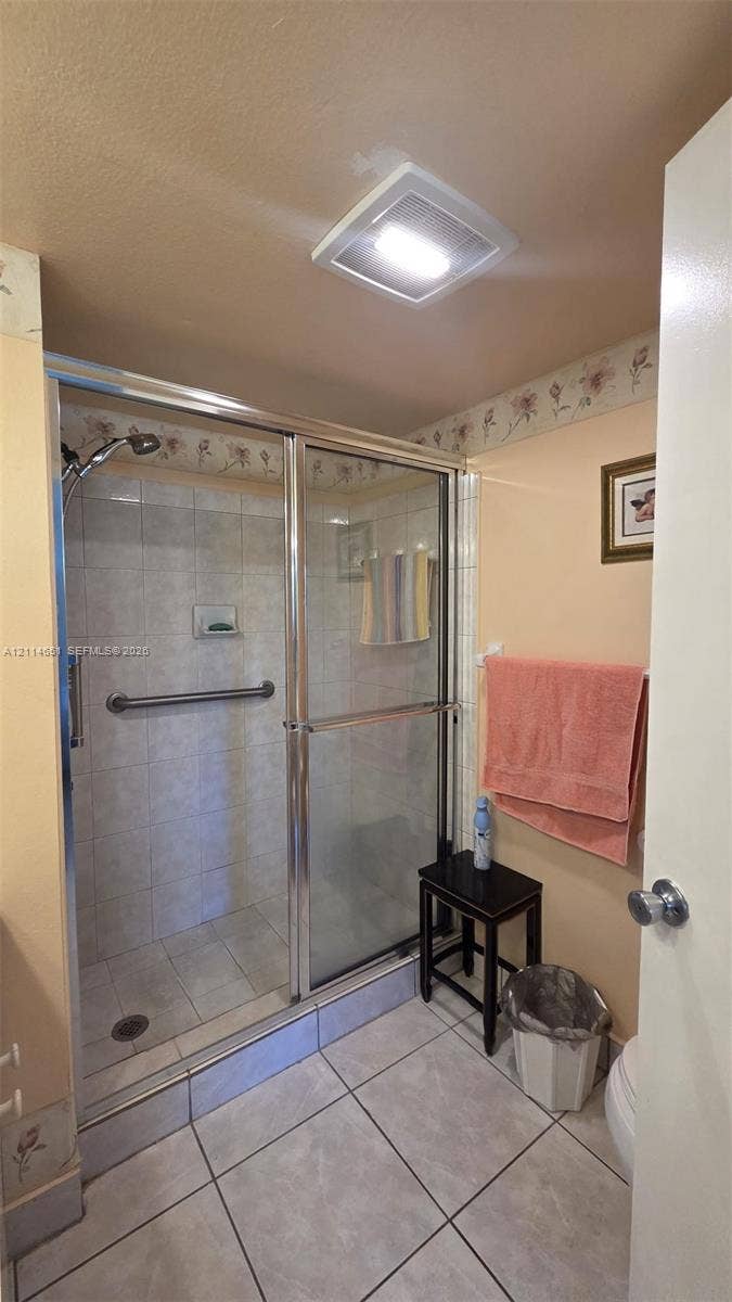 Shower stall featuring a glass-enclosed frame, tiled walls with a built-in recessed soap niche, a mounted metal grab bar, and large-format tile flooring