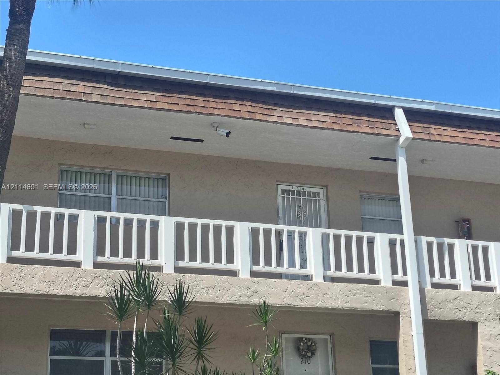 Stucco exterior featuring a second-story balcony with white railing, asphalt shingle roofing, and vertical sliding windows