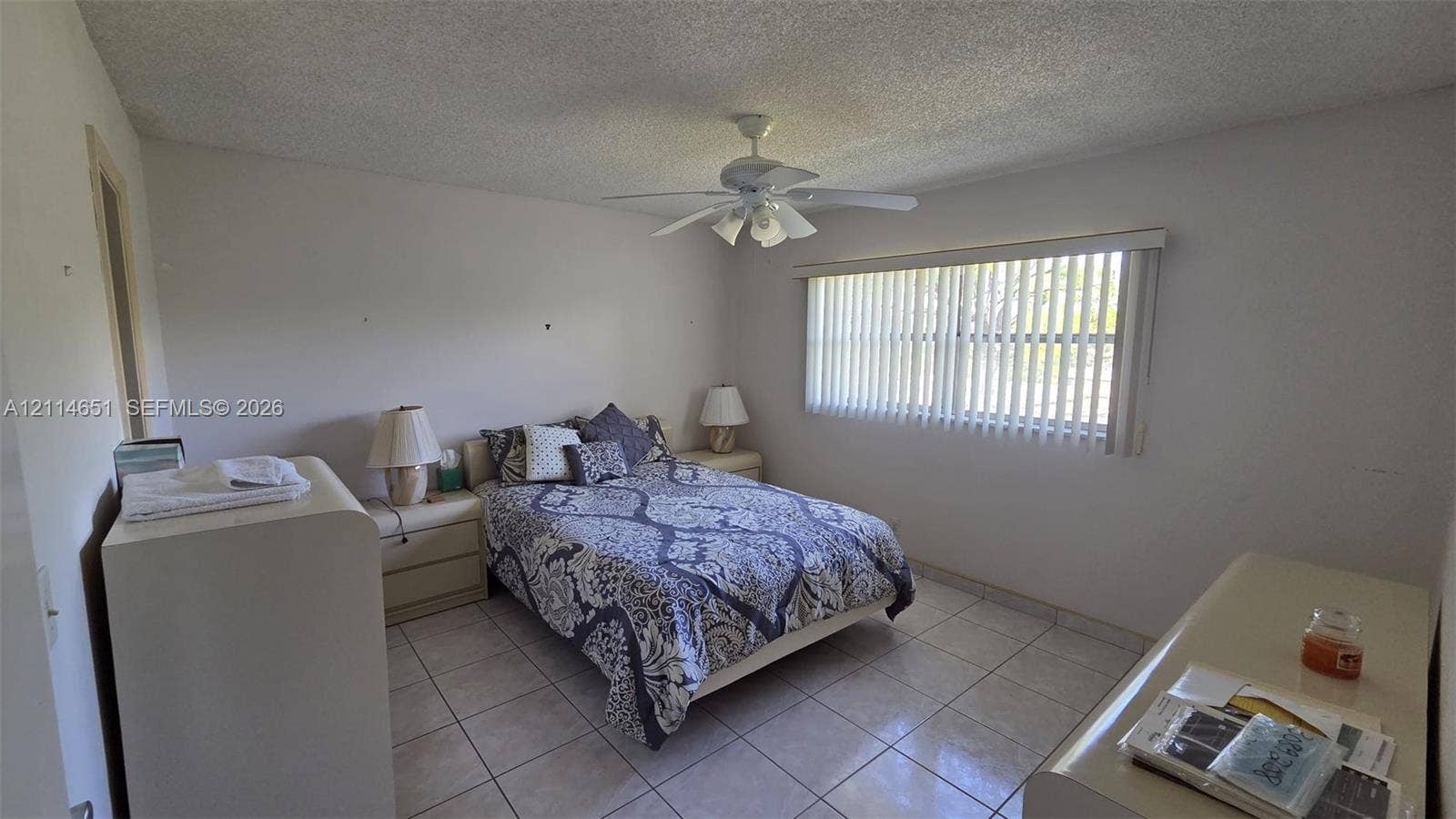 Room featuring light-colored tile flooring, a multi-blade ceiling fan, and vertical window blinds