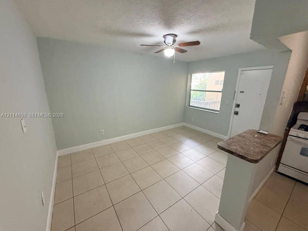 350 E 21st Street, #209, Hialeah, Hialeah, FL 33010 Neutral-toned tile flooring, light-colored walls, ceiling fan with integrated lighting, and a kitchen peninsula with a stone-finish countertop