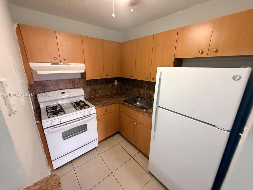 350 E 21st Street, #209, Hialeah, Hialeah, FL 33010 Kitchen featuring wood-finish cabinetry, stone-texture laminate countertops, a stainless steel sink, a white gas range, and ceramic tile flooring