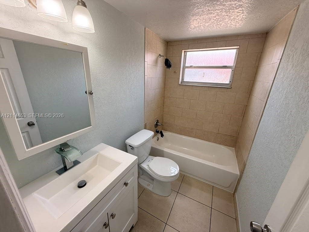 350 E 21st Street, #209, Hialeah, Hialeah, FL 33010 Bathroom featuring a white vanity with a rectangular sink, waterfall faucet, framed wall-mounted mirror, ceramic tile flooring, and a tiled tub surround