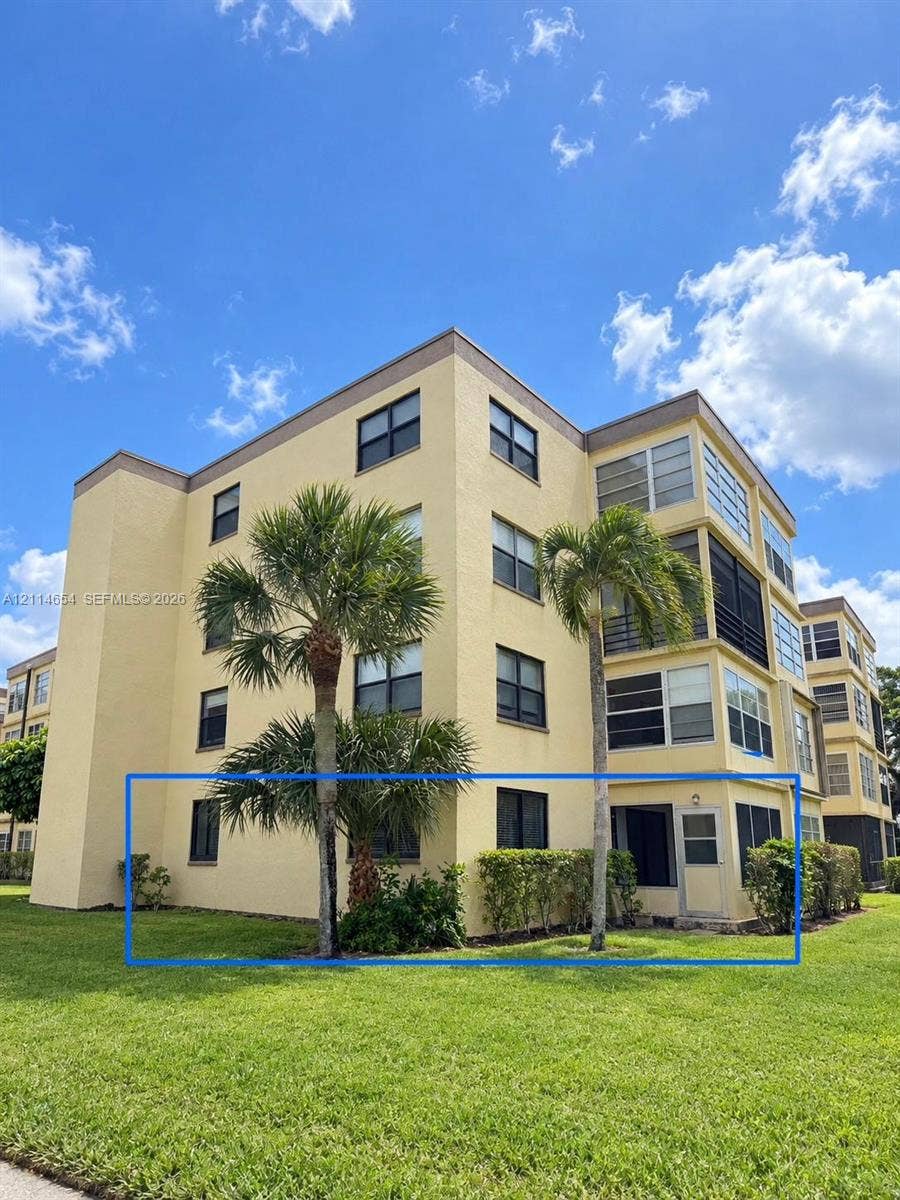 Stucco exterior multi-story building featuring ground-level screened-in patio, lush landscaping, and mature palm trees
