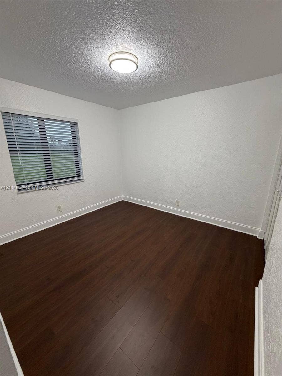 Room featuring wood-finish flooring, textured white walls, a flush-mount ceiling light fixture, and a window with horizontal blinds