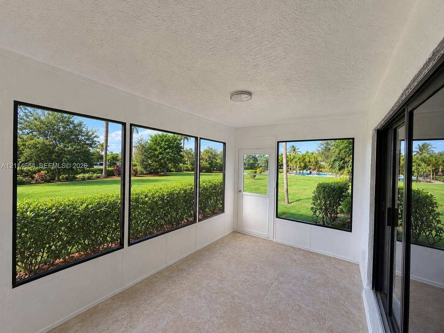 Enclosed sunroom featuring expansive windows with black frames, tile flooring, and a glass-paneled entry door