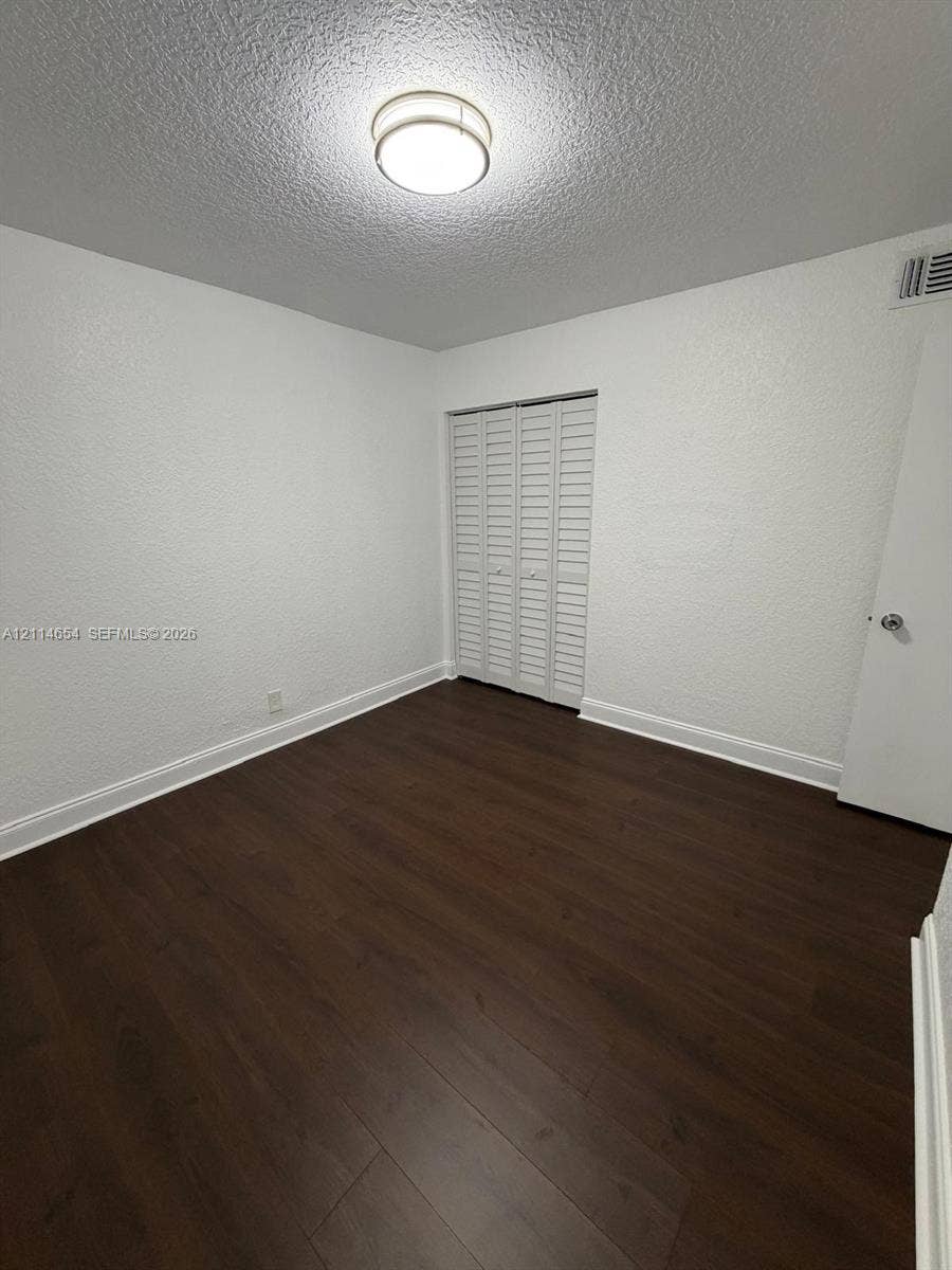 Room featuring dark wood-finish flooring, white textured walls, and a bi-fold louvered closet door