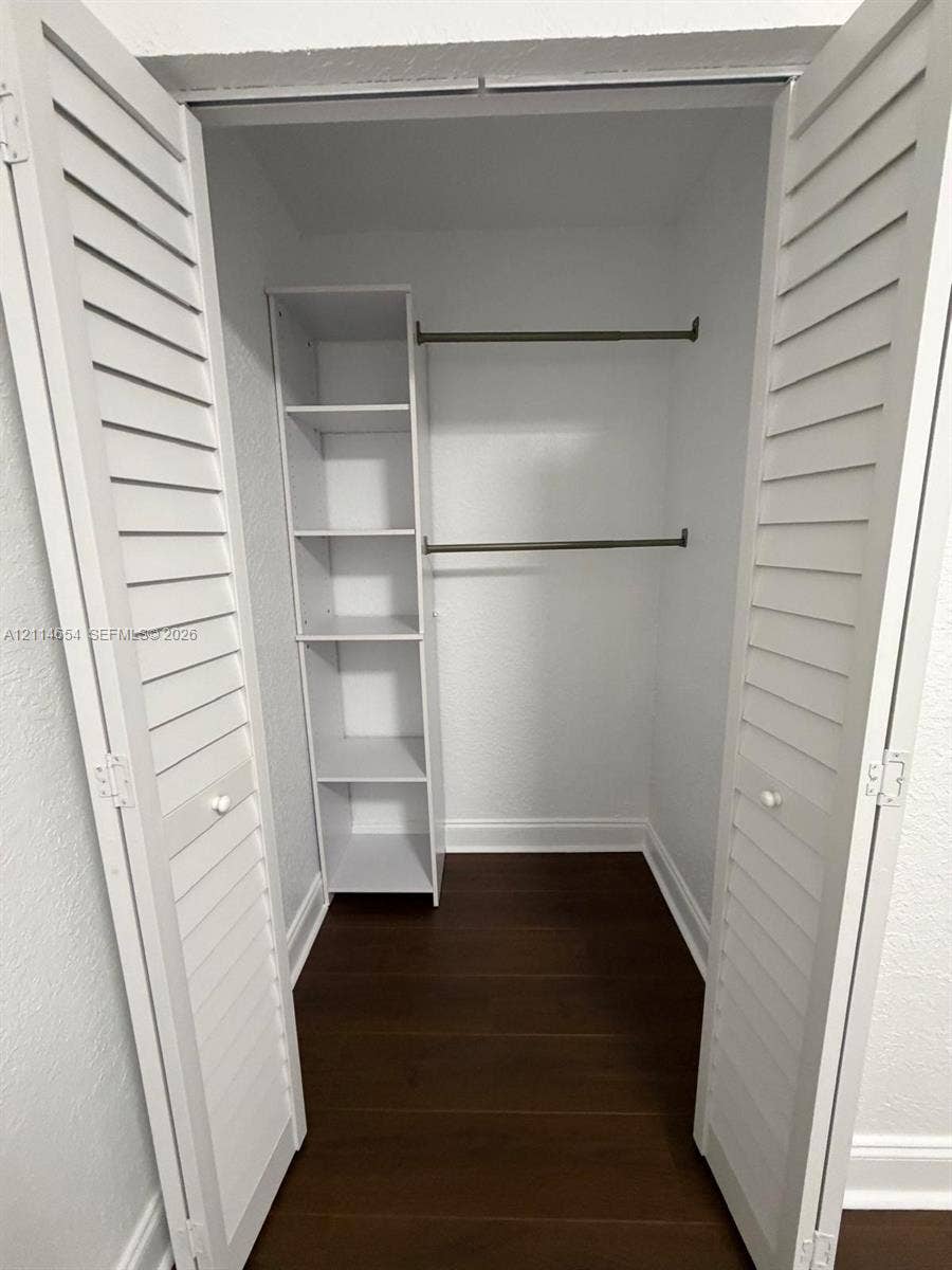 Closet featuring white louvered bifold doors, wood-finish flooring, built-in shelving, and dual metal clothing rods