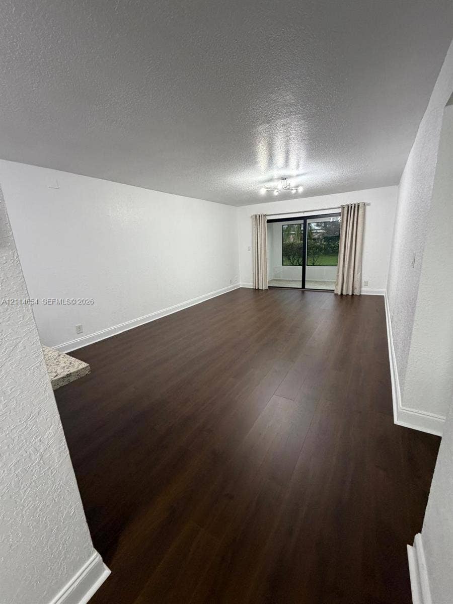 Open-concept interior featuring dark wood-finish flooring, sliding glass door, multi-bulb flush-mount ceiling lighting, and a stone-surface built-in element
