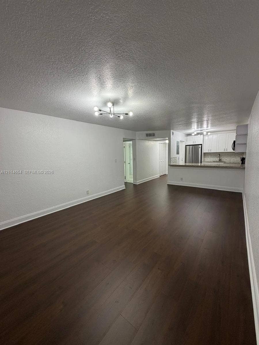 Open-concept interior featuring wood-finish flooring, a contemporary multi-arm chandelier, and a kitchen equipped with white cabinetry, stainless steel appliances, and stone-surface countertops