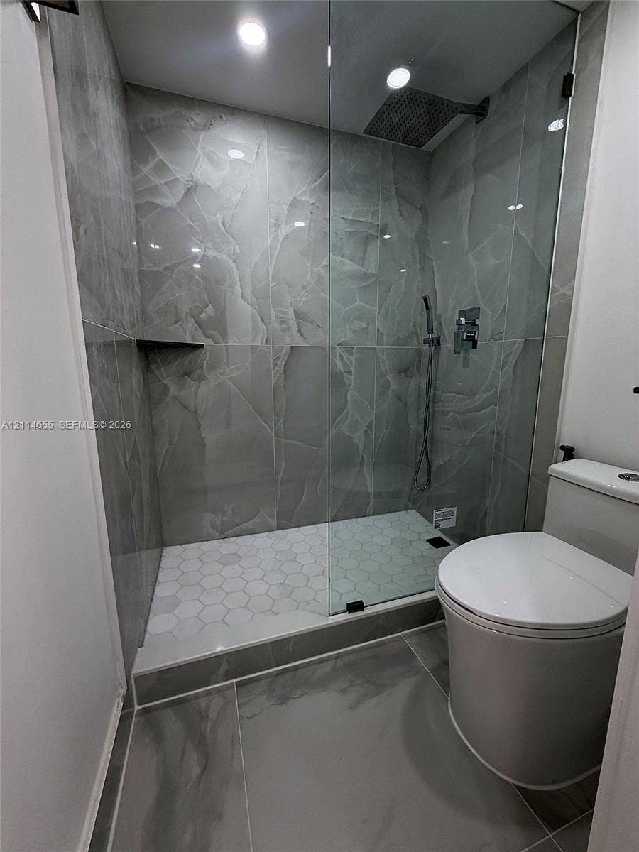 3301 N Country Club Drive, #507, Aventura, Aventura, FL 33180 Walk-in shower featuring large-format stone-look wall tiling, white hexagonal floor tiling, a ceiling-mounted rainfall showerhead, a wall-mounted handheld sprayer, and a recessed corner shelf