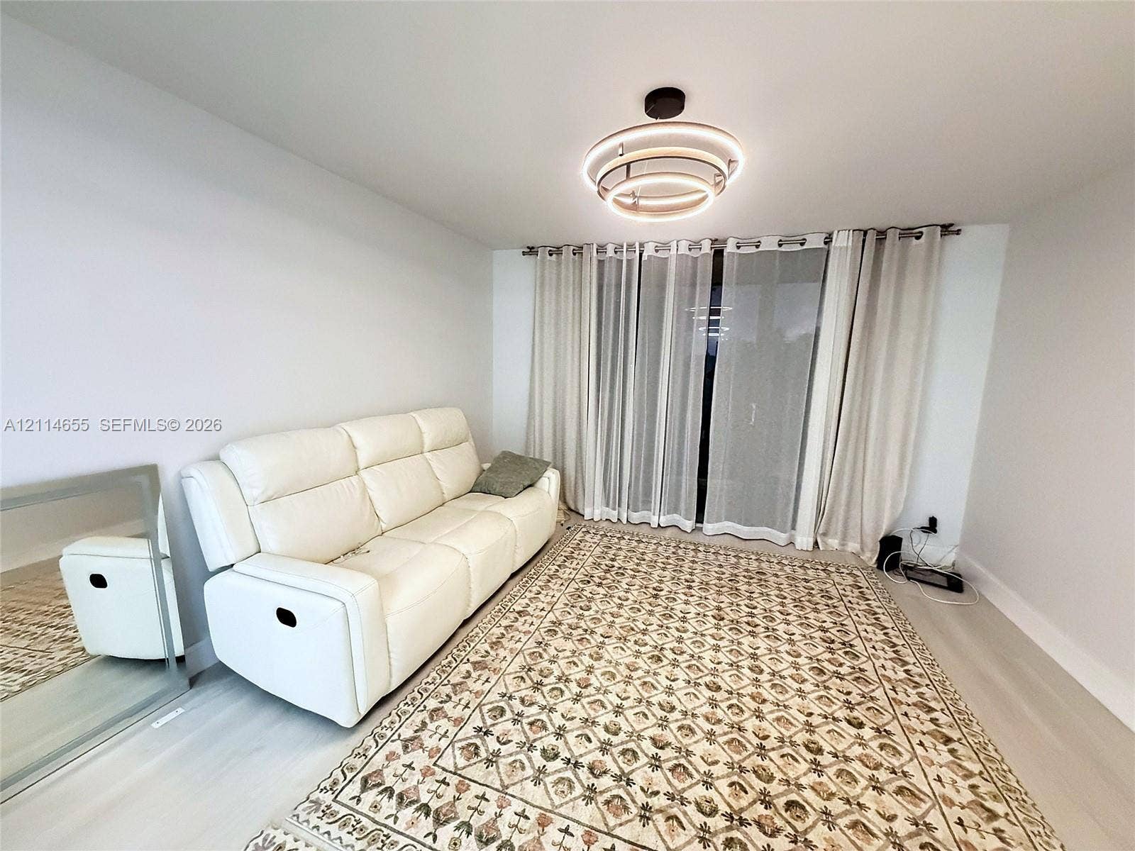 3301 N Country Club Drive, #507, Aventura, Aventura, FL 33180 Modern interior space featuring light-toned wood-finish flooring, a tiered circular LED flush-mount fixture, and full-height sliding glass doors