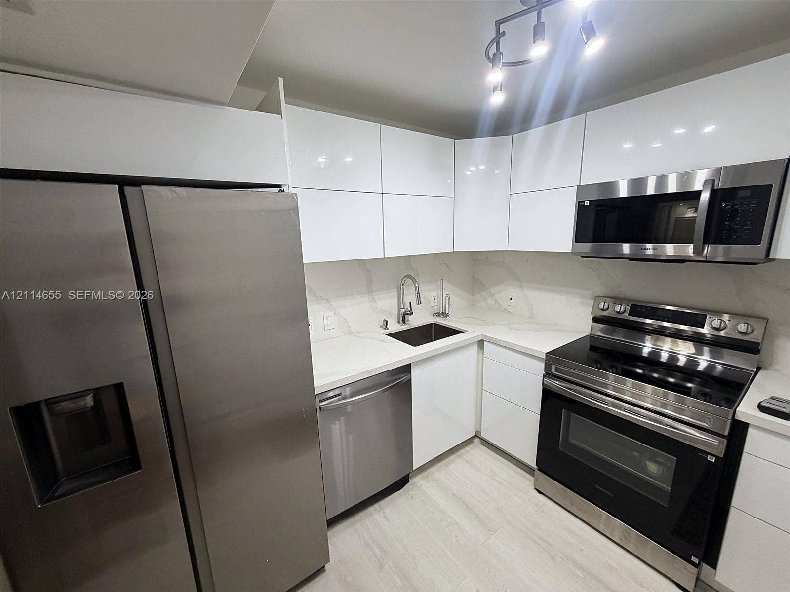 3301 N Country Club Drive, #507, Aventura, Aventura, FL 33180 Kitchen featuring high-gloss white cabinetry, white stone-finish countertops, full-height stone-finish backsplash, stainless steel appliances, and wood-finish flooring