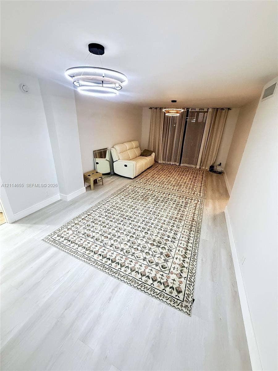 3301 N Country Club Drive, #507, Aventura, Aventura, FL 33180 Interior room featuring light-toned wood-finish flooring, two modern multi-tier LED light fixtures, and floor-to-ceiling curtain panels