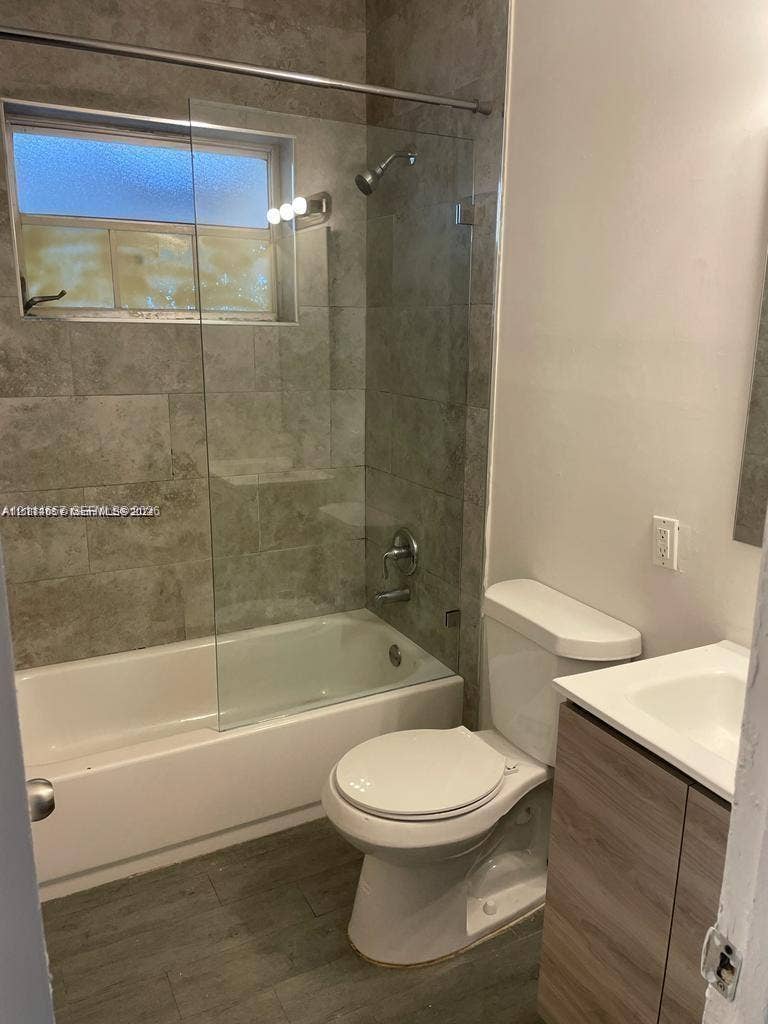 770 NE 123rd Street, #12, North Miami, North Miami, FL 33161 Bathroom featuring large-format tile shower surround, frameless glass shower panel, wood-finish vanity with integrated sink, and wood-finish flooring