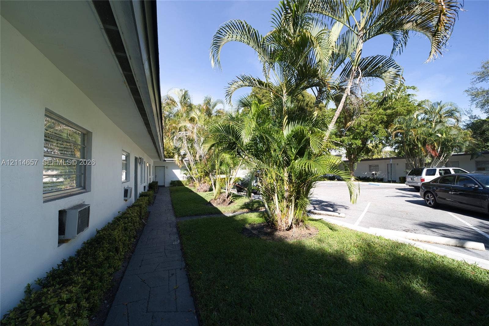770 NE 123rd Street, #12, North Miami, North Miami, FL 33161 Exterior walkway featuring stone-paver paving, manicured lawn areas, mature palm trees, and asphalt surface parking
