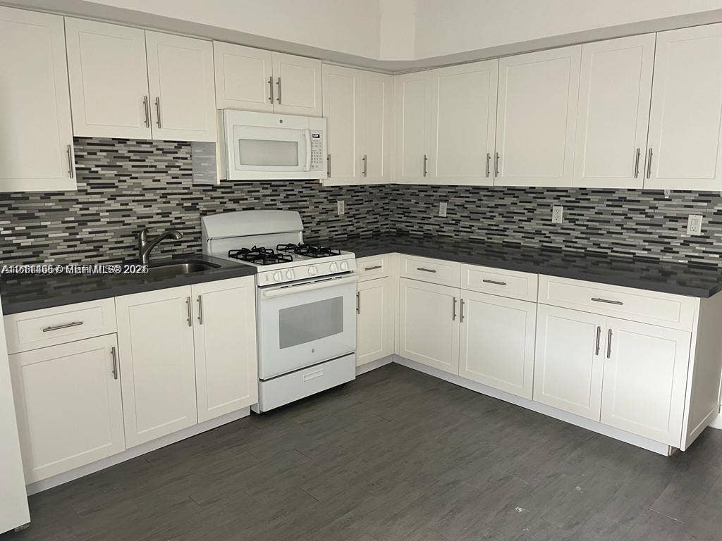 770 NE 123rd Street, #12, North Miami, North Miami, FL 33161 Kitchen featuring white shaker-style cabinetry, dark stone-finish countertops, linear tile backsplash, wood-finish flooring, and white built-in appliances