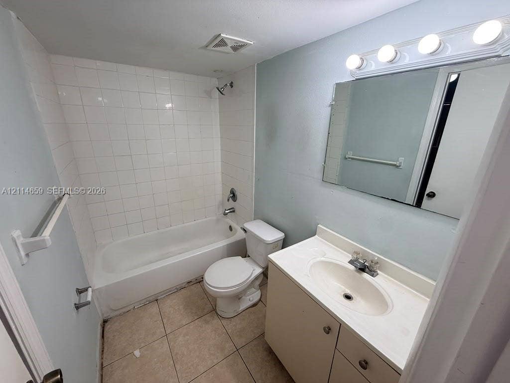 Bathroom featuring tile flooring, a tub-shower combination with full-height tile surround, vanity with integrated basin, and wall-mounted vanity lighting