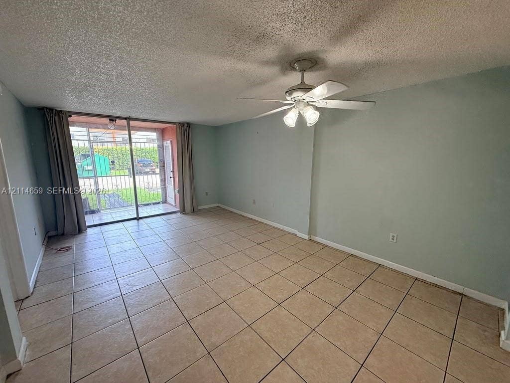 Living area featuring neutral ceramic tile flooring, a multi-light ceiling fan, and sliding glass doors leading to an exterior patio with security bars