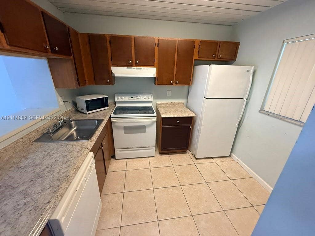 Kitchen featuring wood cabinetry, laminate countertops, a stainless steel sink, ceramic tile flooring, and a window with blinds