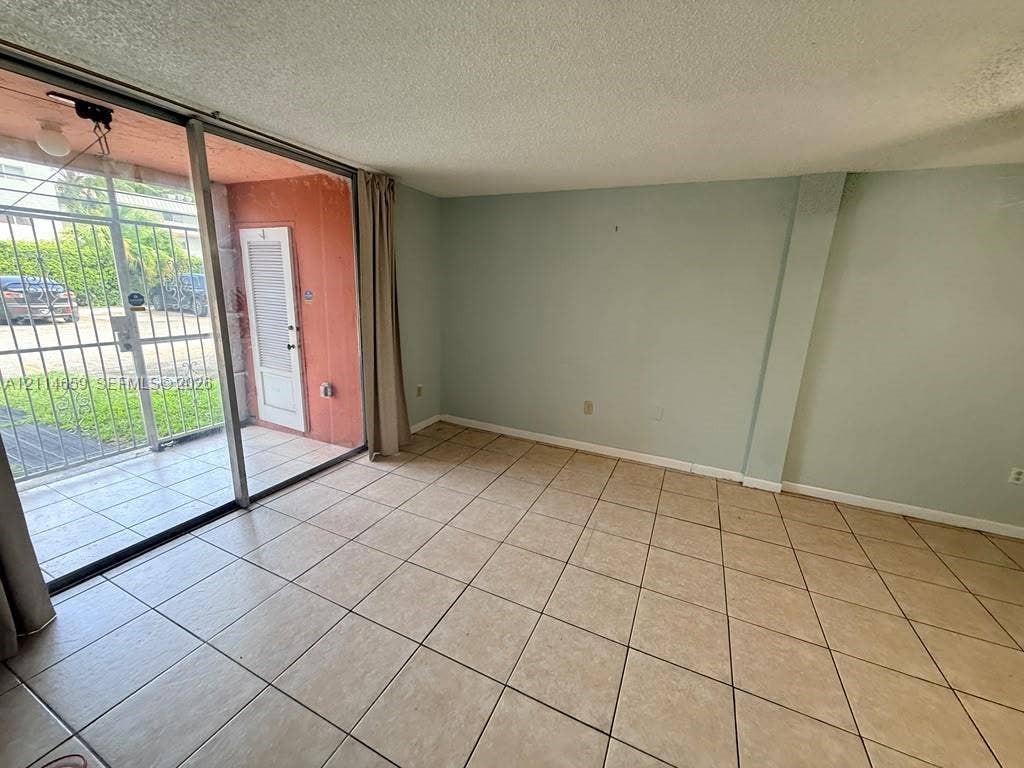 Interior space featuring large-format ceramic tile flooring, sliding glass patio door, and exterior metal security gate
