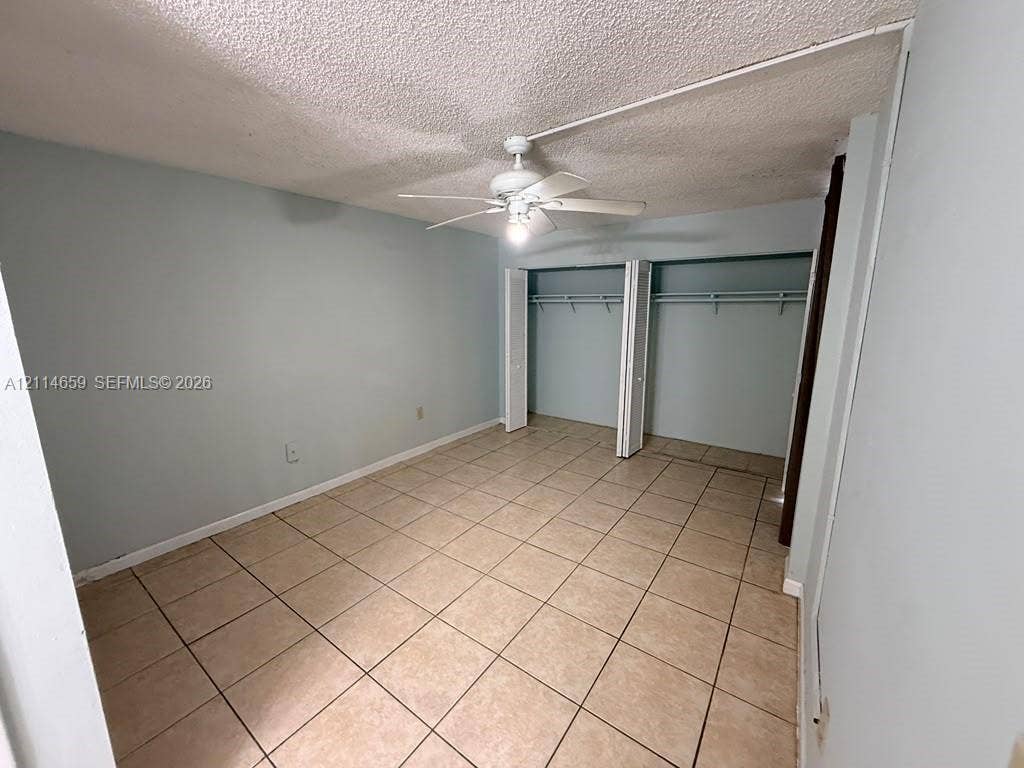 Room featuring neutral-toned tile flooring, ceiling-mounted fan with light fixture, and walk-in closet with double bifold doors