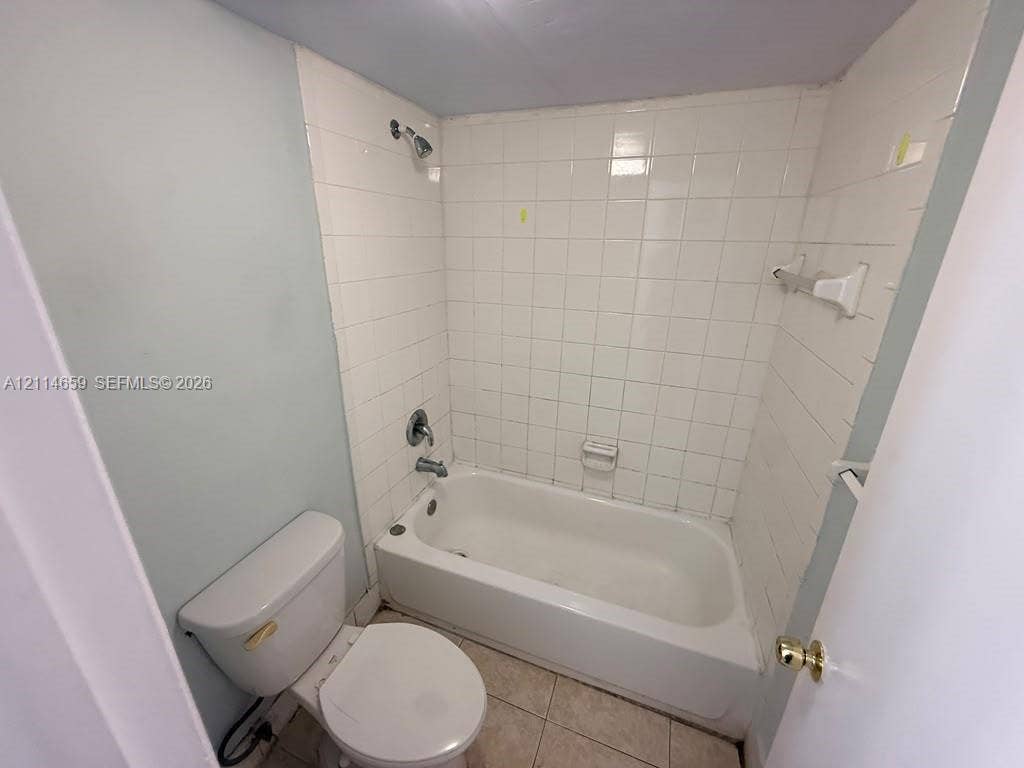 Full bathroom featuring a white porcelain soaking tub, tile surround, wall-mounted shower head, and tile flooring
