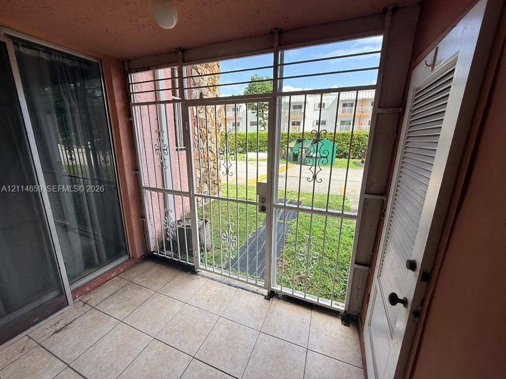 Enclosed patio featuring large-format tile flooring, a white louvered door, metal security screening with decorative ironwork, and a sliding glass door