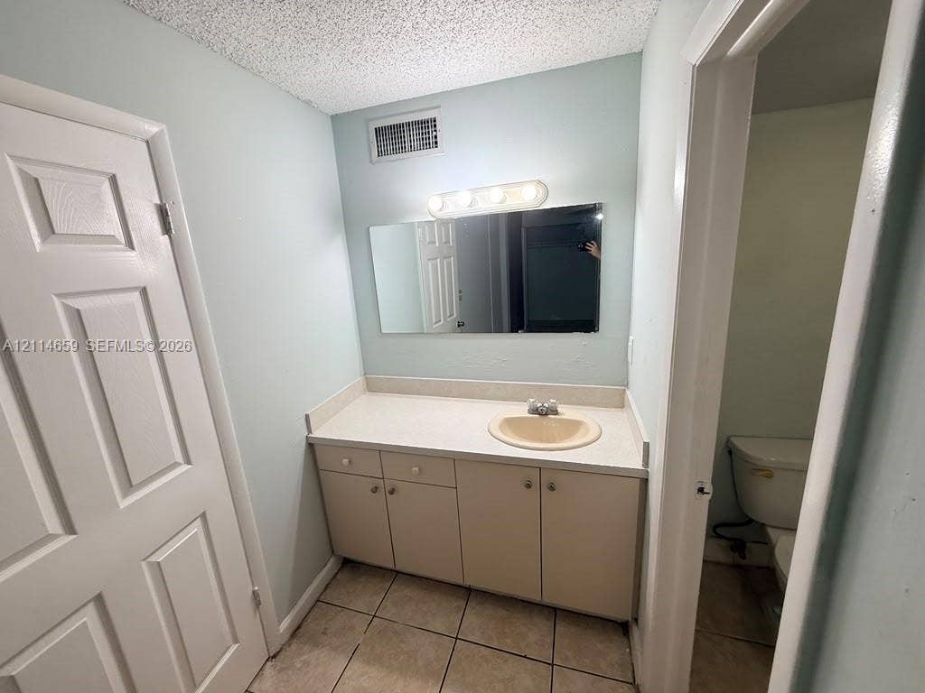 Vanity with integrated sink and countertop, rectangular wall mirror, four-light vanity fixture, and tiled flooring